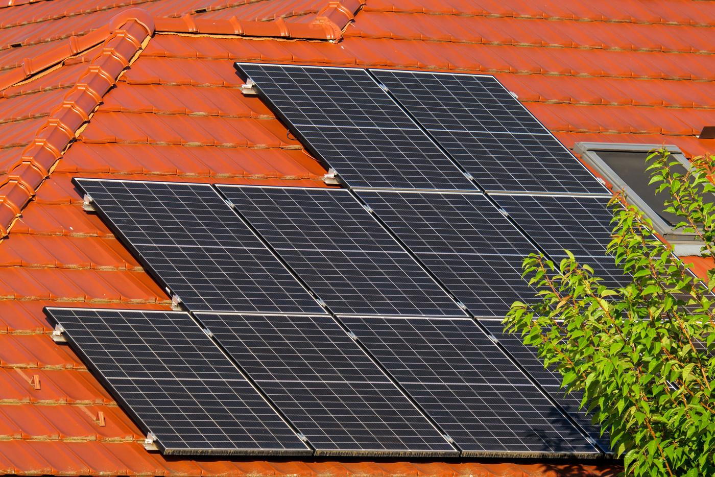 Módulos fotovoltaicos fixados com ganchos e grampos sobre um telhado de telhas cerâmicas vermelhas, em dia de sol
